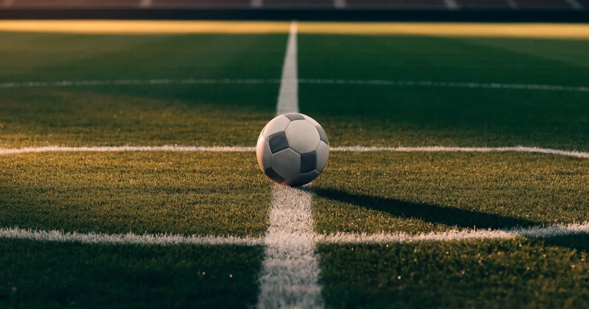 Ein Fussball liegt auf dem Mittelkreis eines Rasenfelds, die weissen Linien kreuzen sich auf dem gepflegten Gras im warmen Abendlicht.