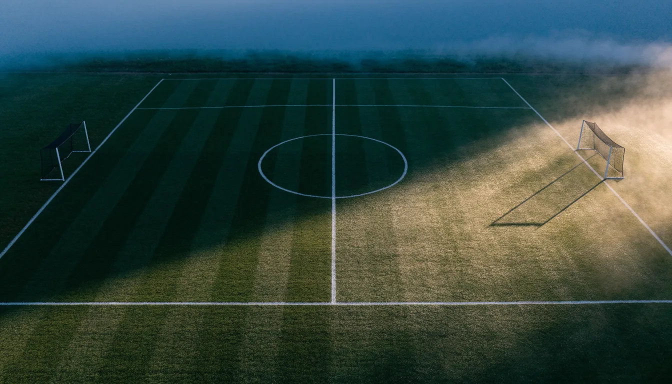 Ein Fussballplatz von oben gesehen, die Linien bilden ein helles Muster auf dem Rasen, Drohnenperspektive in der Morgendämmerung.