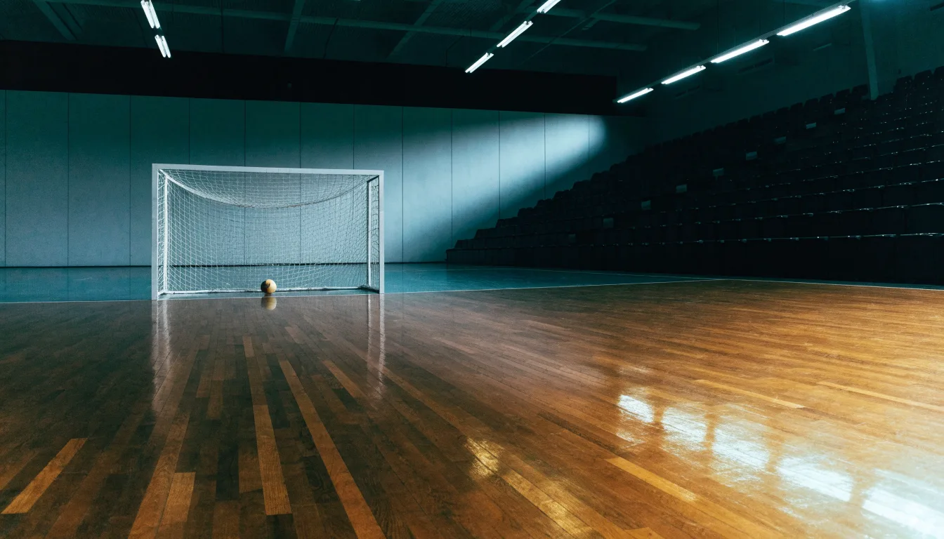 Ein Handballtor in einer leeren Sporthalle, der Ball liegt im Torraum und das Hallenlicht spiegelt sich im Parkett.