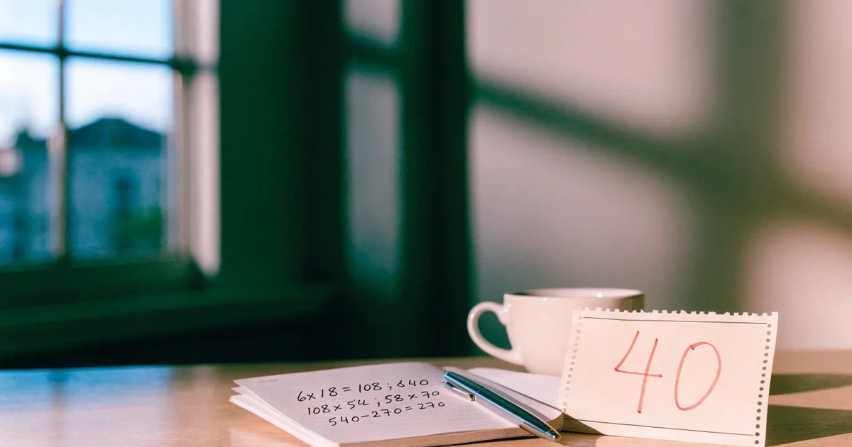 Ein Taschenrechner und ein Bleistift liegen auf kariertem Papier neben einer Tasse Kaffee, ein Fensterplatz mit Tageslicht.