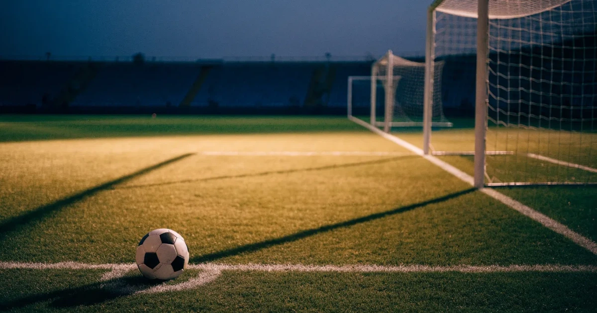 Ein Fussballplatz im Abendlicht mit langen Schatten der Torpfosten, die Rasenfläche leuchtet gelblich.