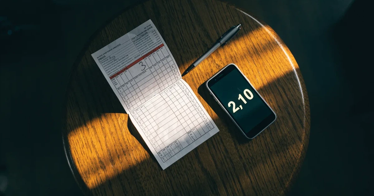 Eine leere Geldbörse aus Leder liegt geöffnet auf einem Tisch, daneben ein Kugelschreiber und ein Smartphone mit dunklem Display.